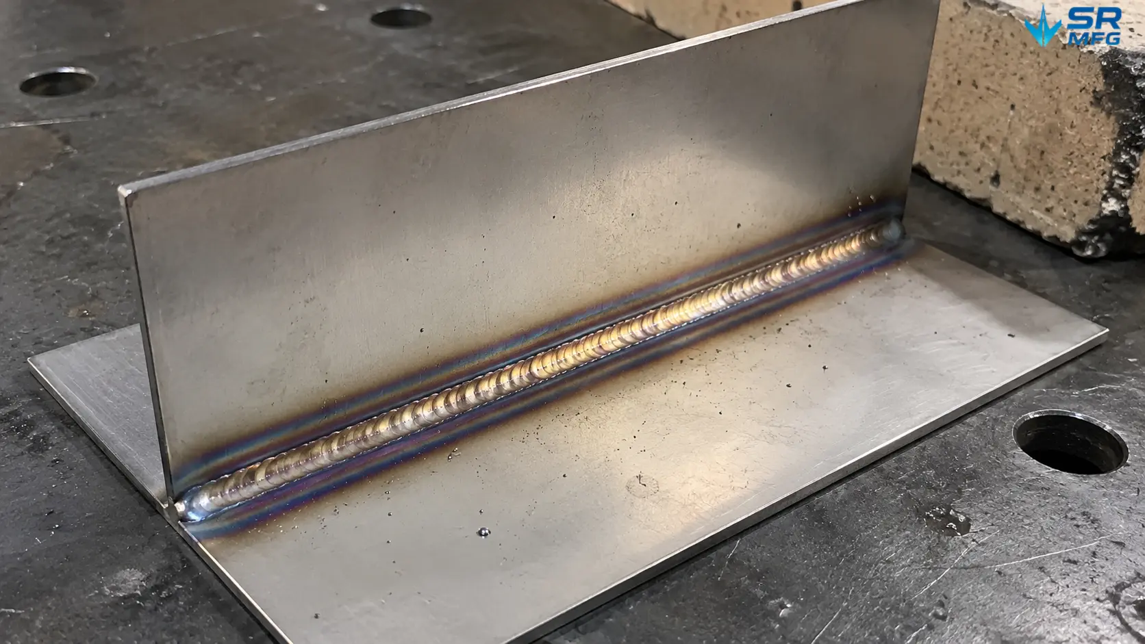 TIG-welded 2mm stainless steel sheet joint showing heat discoloration bands ranging from straw yellow to purple blue around the weld bead
