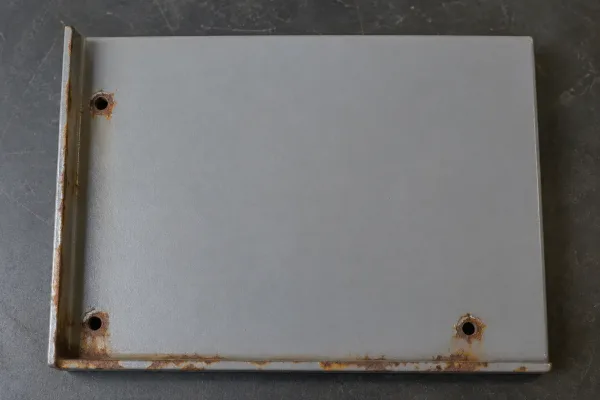 Powder-coated steel panel with brown rust spots along bent edges and mounting holes