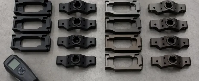 Black anodized aluminum parts arranged on an inspection surface next to color variation samples showing inconsistent black tones