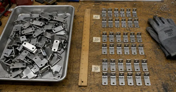 Small sheet metal brackets counted into groups of ten on a workbench, separated by a physical divider from uncounted parts