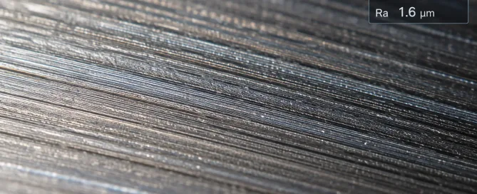 Close-up macro photograph of a machined metal surface showing visible tool marks, roughness peaks and valleys, with a surface roughness measurement readout overlay